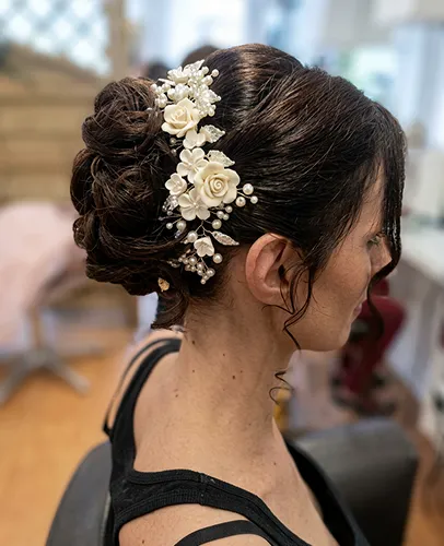 Coiffure élégante avec fleurs et perles sur chignon sophistiqué.